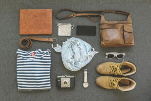 Vintage travel essentials flat lay with leather bags, shoes, camera, and clothing.